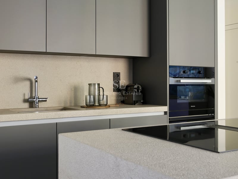 Cuisine minimaliste avec placards gris mat, plans de travail en pierre sable et four Miele encastré.