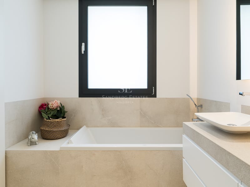 Salle de bain minimaliste avec baignoire blanche, vasque sur plan en pierre et fenêtre à cadre noir.