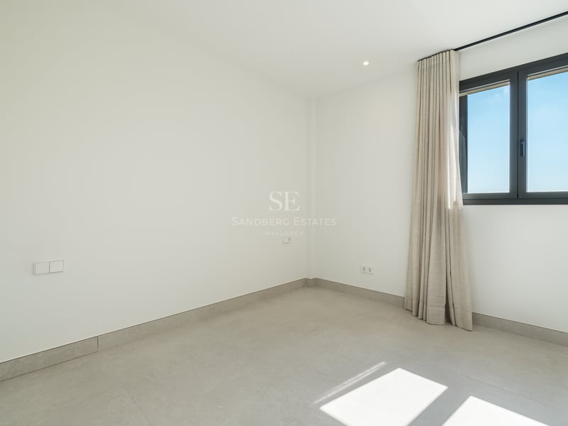 Habitación vacía de estilo minimalista con paredes blancas, suelos de porcelánico gris y ventana con cortinas neutras.