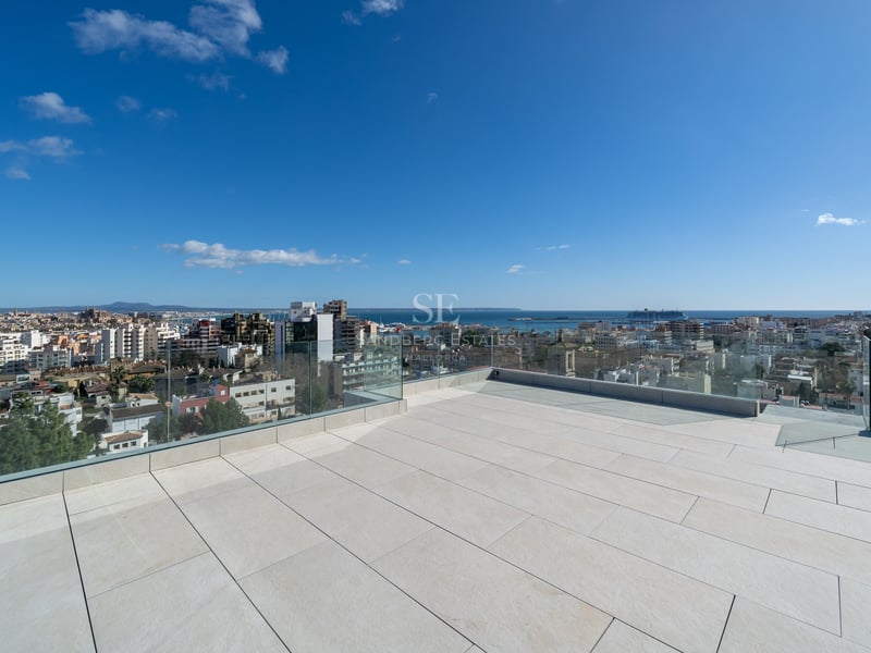 Grande terrasse sur le toit avec carrelage en pierre claire et garde-corps en verre surplombant Palma et la mer.