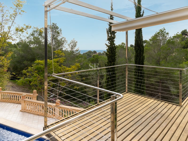 Terrasse surélevée en bois avec garde-corps métalliques surplombant une piscine et une forêt luxuriante.