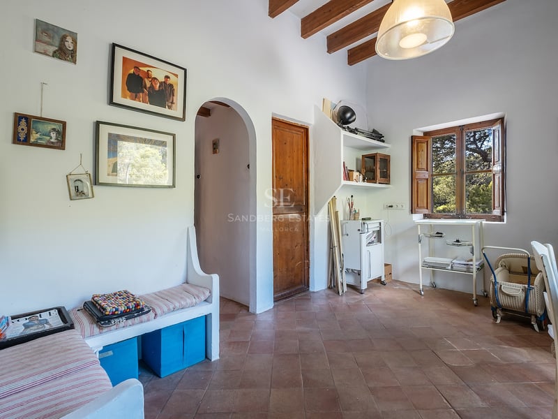 Pièce intérieure avec carrelage en terre cuite, poutres en bois au plafond, murs blancs et banquette intégrée.
