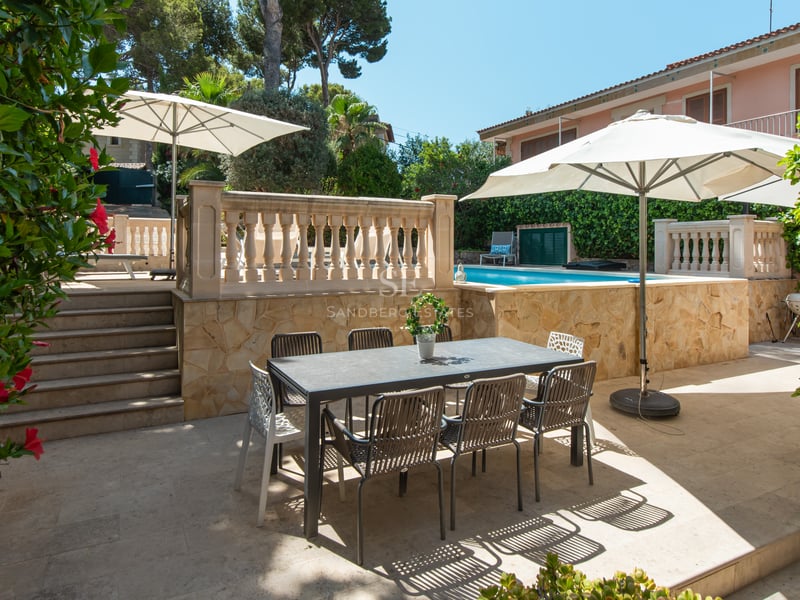 Terrasse avec table à manger sombre et parasols blancs à côté d'une piscine surélevée bleu turquoise.