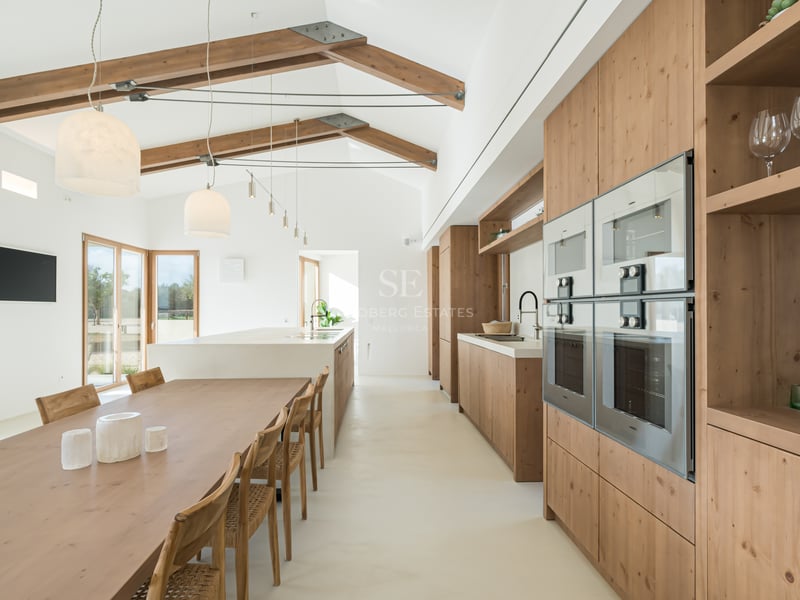 Bright open-plan kitchen and dining area with high vaulted ceilings, exposed wooden beams, and natural oak cabinetry.
