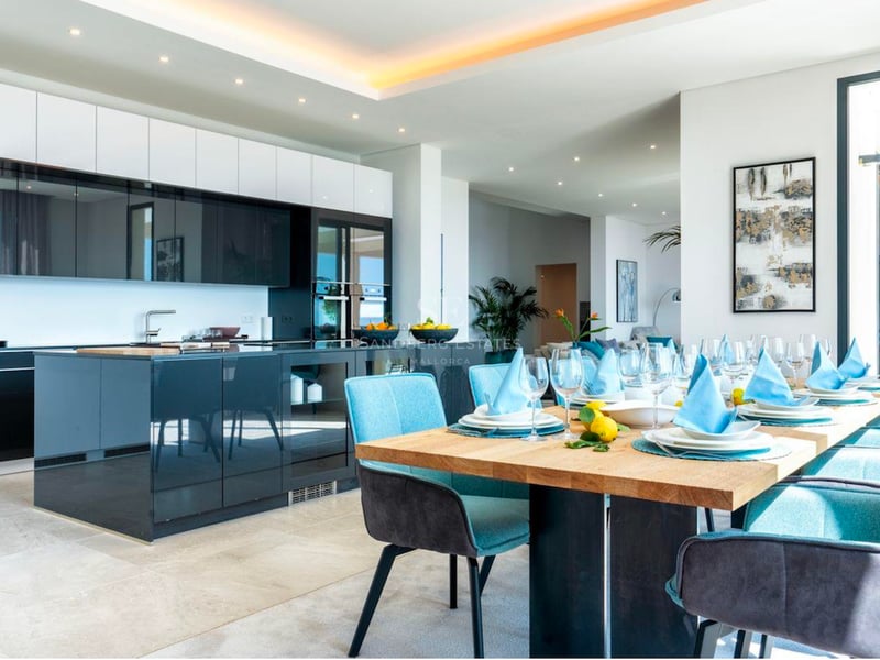 Cuisine moderne haut de gamme avec îlot bleu foncé et table à manger en bois avec chaises turquoise.