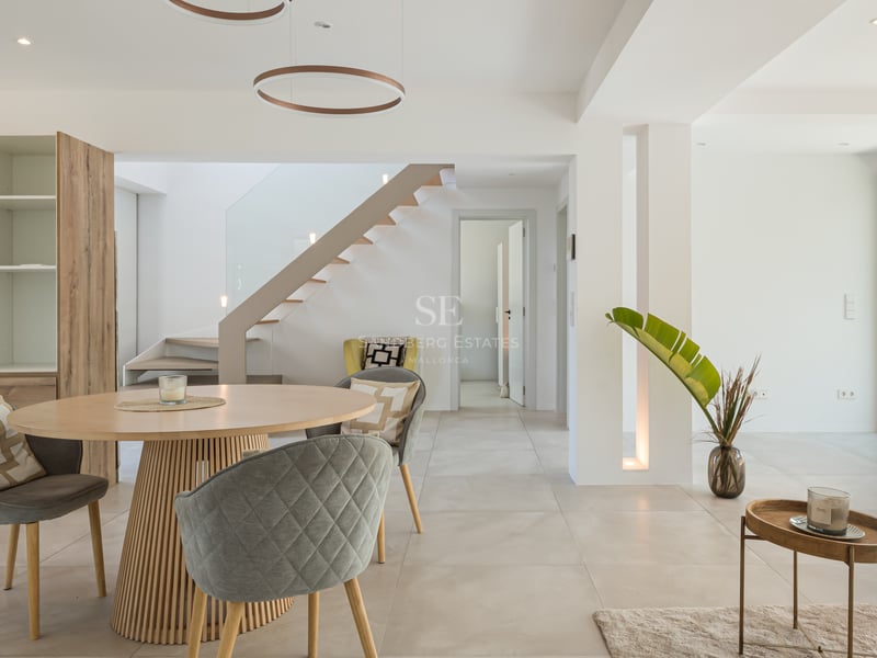 Salle à manger contemporaine avec table ronde en bois, chaises grises et escalier suspendu près des baies vitrées.
