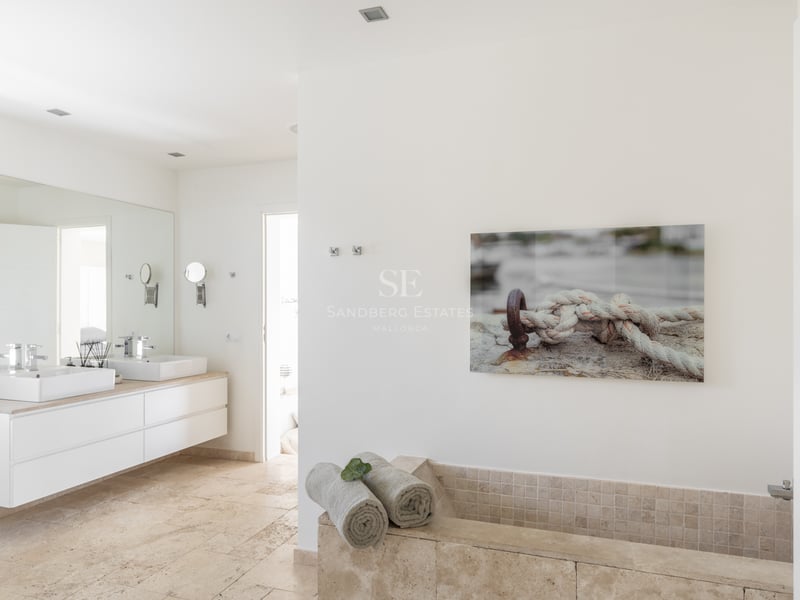 Salle de bains lumineuse avec double vasque suspendue, sol en travertin et baignoire intégrée en pierre.