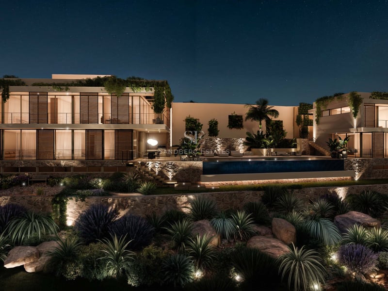 Vue nocturne d'une villa de luxe avec piscine éclairée, murs en pierre naturelle et baies vitrées.
