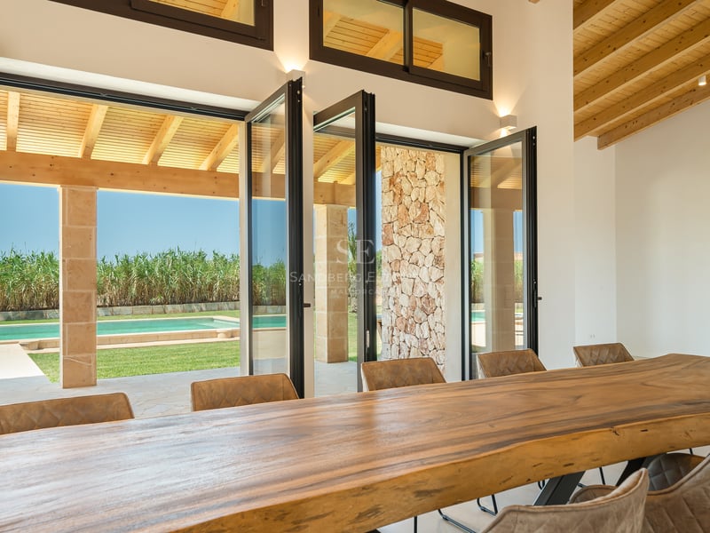 Gran mesa de madera maciza frente a puertas de cristal plegables que dan al jardín y la piscina.