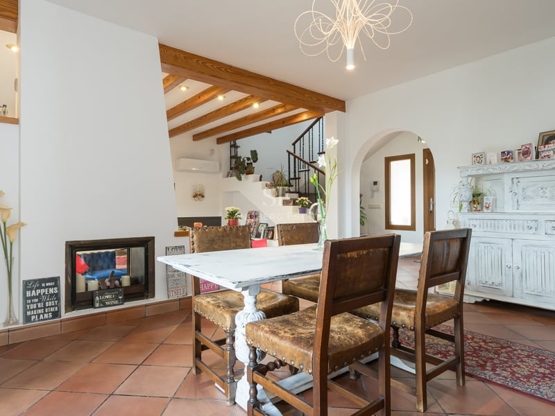 Intérieur d'une salle à manger avec sol en terre cuite, poutres en bois, table blanche vieillie et chaises en cuir.