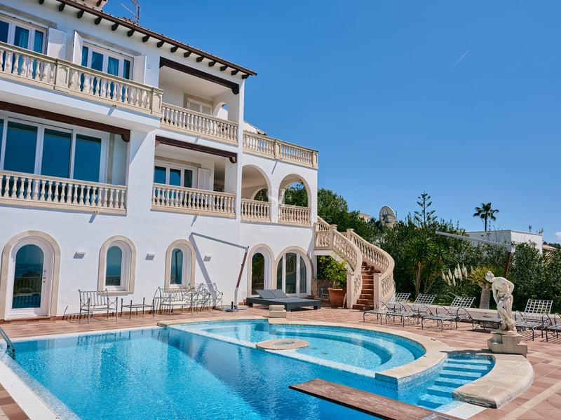 Grande villa blanche à plusieurs niveaux avec piscine bleue courbe, balustrades en pierre et terrasse en terre cuite.