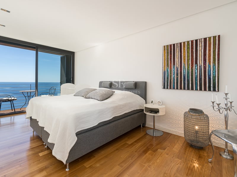 Chambre moderne avec parquet en bois et baies vitrées ouvrant sur un balcon face à la mer.