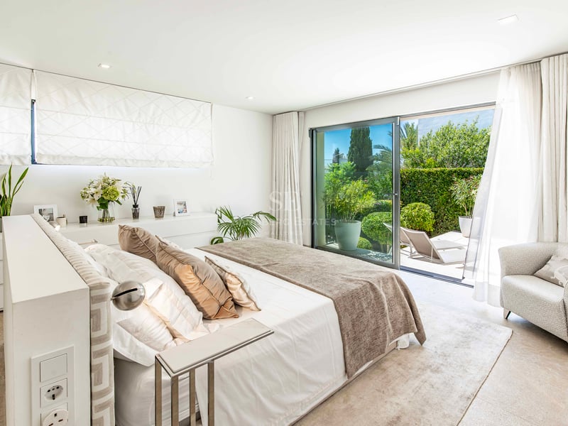 Chambre principale moderne avec baies vitrées coulissantes ouvrant sur une terrasse luxuriante avec chaises longues.