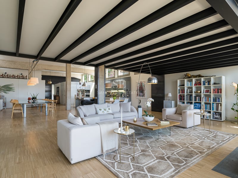 Grand salon avec poutres en acier noir, parquet clair et canapés blancs dans une villa de luxe décloisonnée.