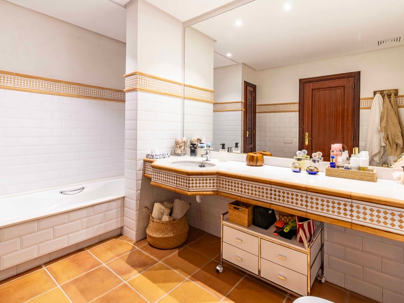 Salle de bain avec carrelage métro blanc, sol en terre cuite, baignoire intégrée et un grand miroir au-dessus du lavabo.
