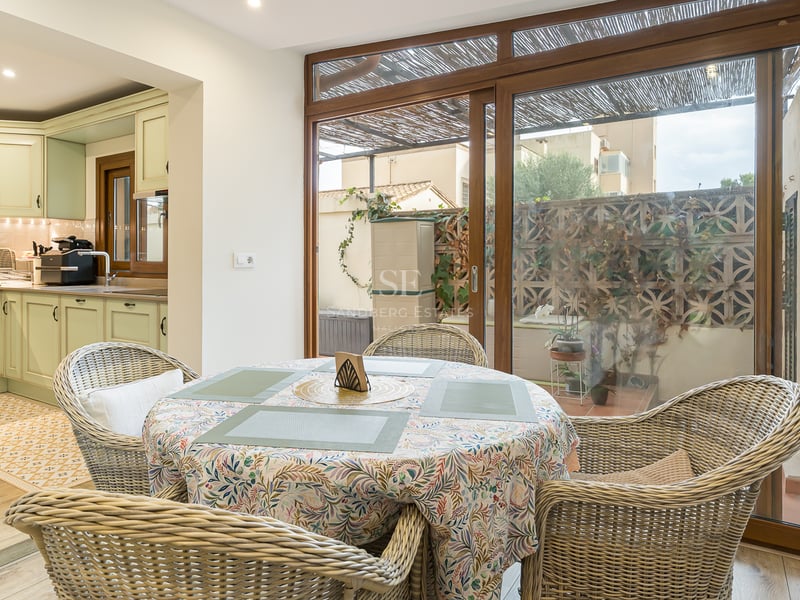 Table à manger avec chaises en osier à côté d'une cuisine vert sauge et de grandes baies vitrées coulissantes.