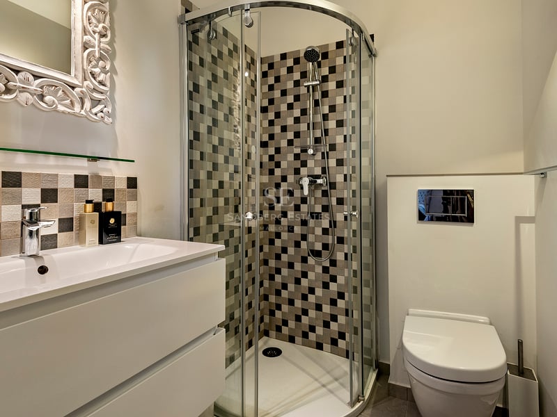 Salle de bain moderne avec une douche en verre, carrelage en damier, lavabo blanc et miroir orné blanc.