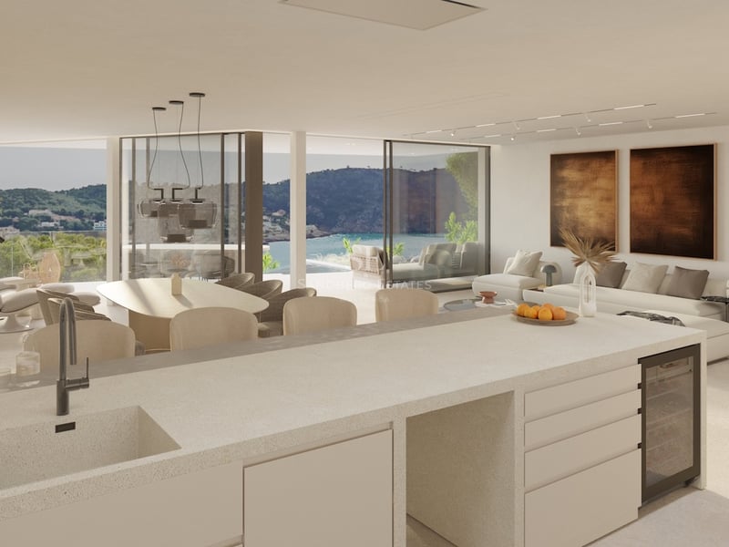 Grand salon ouvert avec cuisine, cheminée suspendue et baies vitrées offrant une vue imprenable sur la côte.