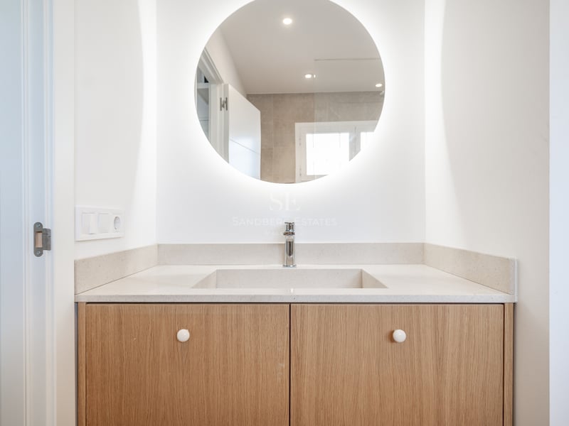 Vanité de salle de bain moderne avec miroir LED circulaire, ébénisterie en bois clair et lavabo blanc.