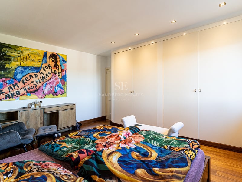 Chambre lumineuse avec placards blancs, parquet en bois, tableau coloré et fauteuil gris.