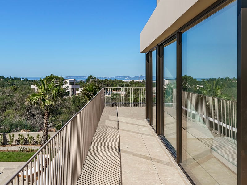 Balcon contemporain avec baies vitrées, garde-corps métallique et vue mer sous un ciel bleu clair.