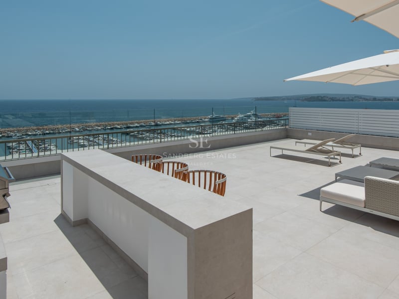 Grande terrasse sur le toit avec cuisine extérieure en inox, salon de jardin et vue sur le port de plaisance.