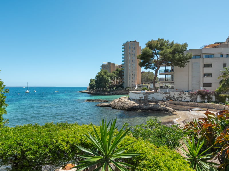 Baie turquoise avec rivages rocheux et bâtiments modernes encadrés par une végétation méditerranéenne luxuriante.