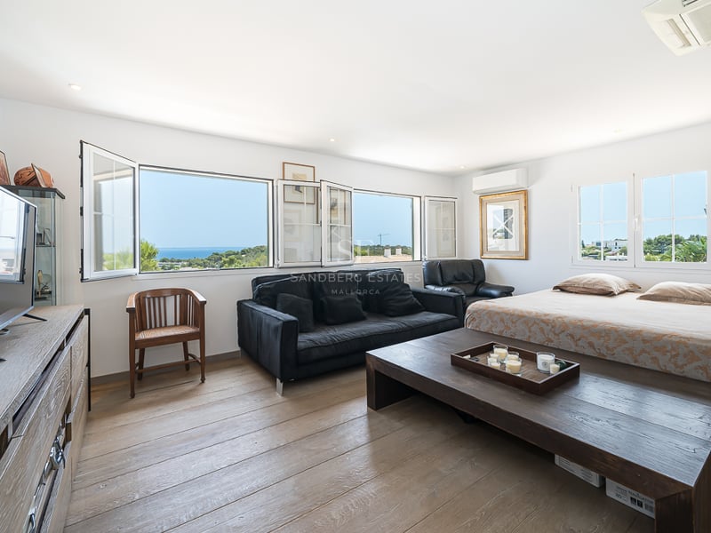 Grande chambre parentale avec parquet en chêne, mobilier en bois sombre et fenêtres donnant sur la mer Méditerranée.