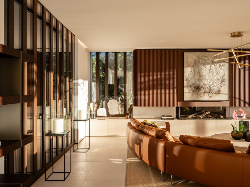 Salon moderne avec canapé en cuir courbé, mur en lattes de bois, cheminée linéaire et lumière naturelle.