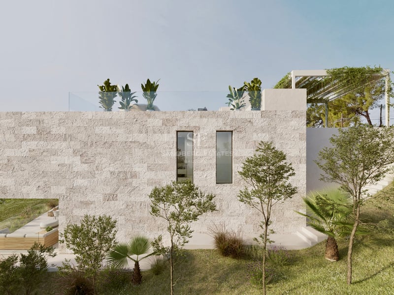 Vue latérale d'une villa de luxe avec murs en pierre texturée, terrasse sur le toit et jardin méditerranéen.