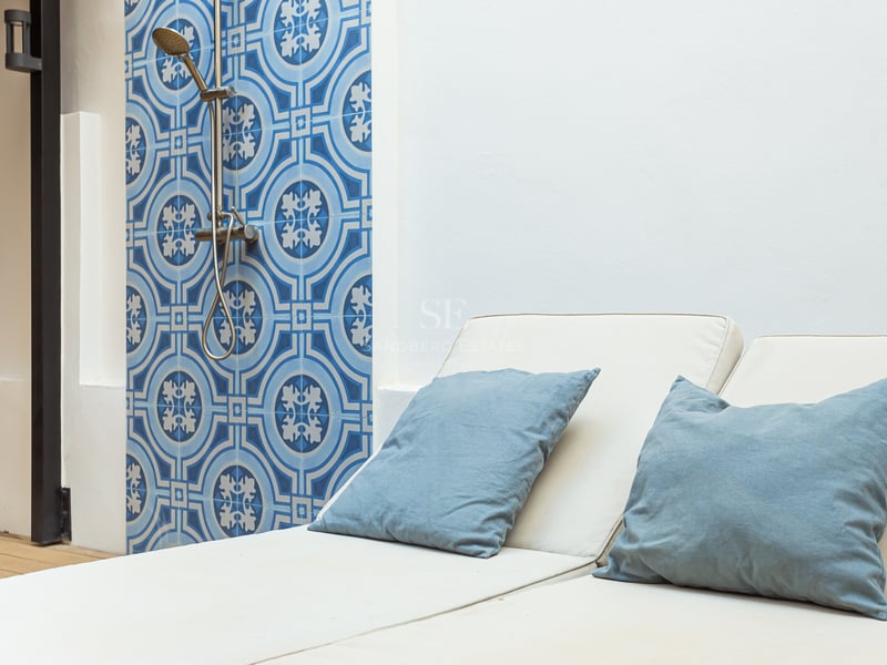 Chaise longue avec coussins bleus à côté d'un mur en carreaux bleus et d'une douche extérieure moderne.