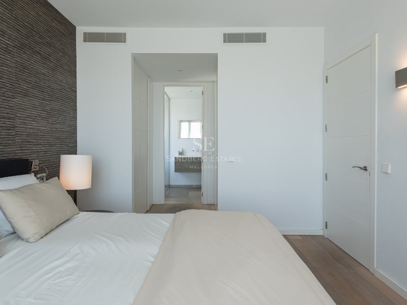 Chambre parentale contemporaine avec mur d'accent en bois sombre, lit blanc et vue sur la salle de bain attenante.