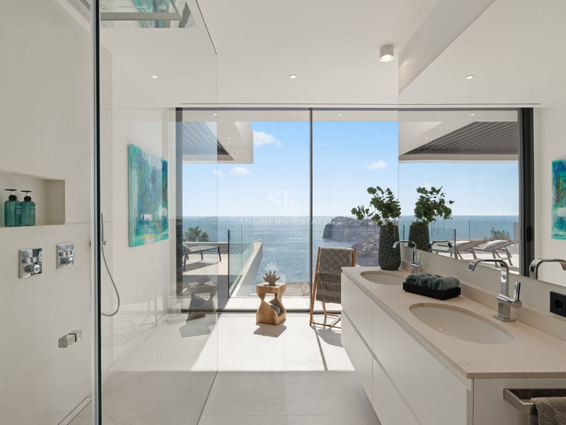 Salle de bain moderne avec douche vitrée et double vasque offrant une vue panoramique sur la mer.