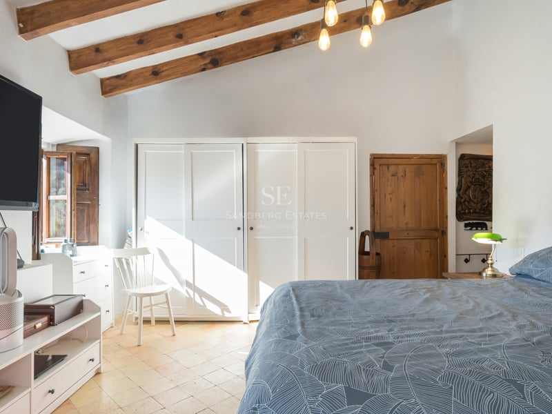 Chambre lumineuse avec poutres de plafond en bois, armoires encastrées blanches et parquet clair.
