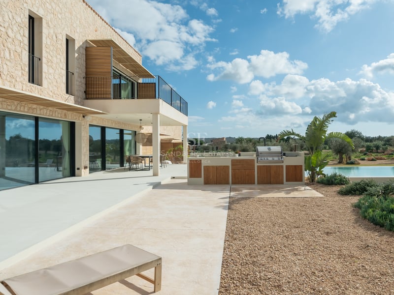 Terrasse moderne avec cuisine d'été en bois, façade en pierre naturelle et larges baies vitrées.