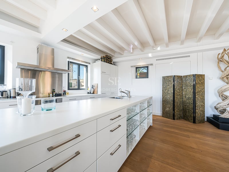 Cuisine blanche moderne avec grand îlot, parquet, poutres au plafond et une sculpture décorative en bois.