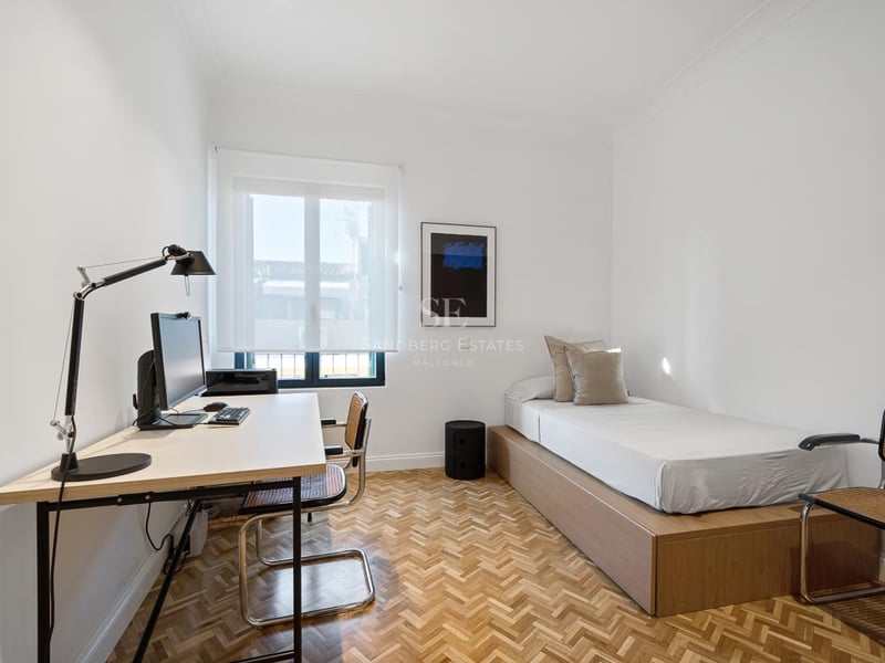 Chambre lumineuse avec lit simple, parquet en chevrons et bureau avec ordinateur.