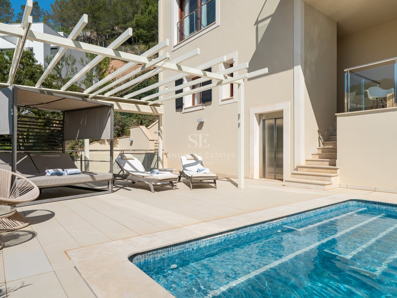Terrasse de villa moderne avec piscine en mosaïque bleue, lits de repos et revêtement en pierre claire.