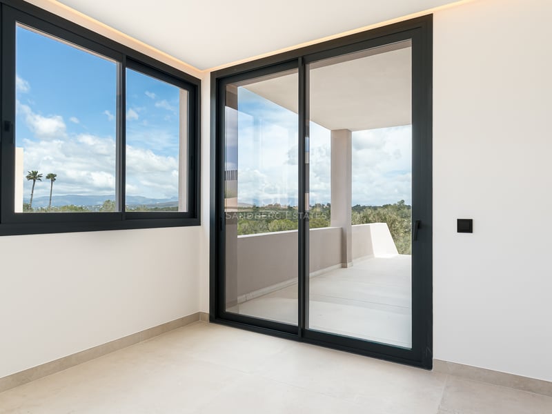 Pièce lumineuse avec grandes baies vitrées coulissantes à cadre noir ouvrant sur une terrasse privée ensoleillée.