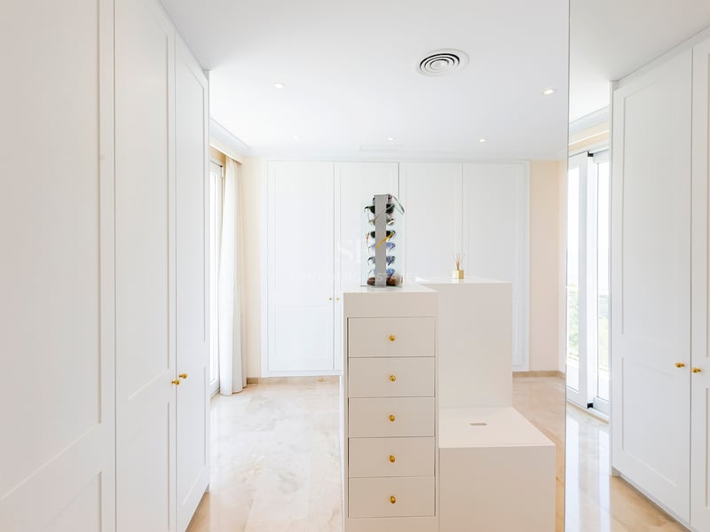 Dressing blanc moderne avec placards intégrés, îlot central et sol en marbre sous une lumière naturelle.