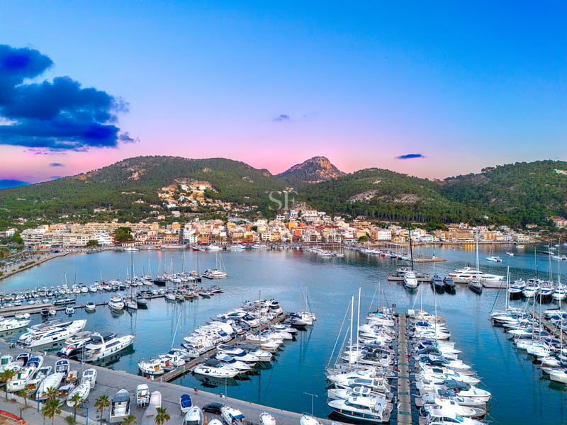 Vue aérienne d'un port de plaisance de luxe avec des yachts blancs sous un ciel rose et bleu et des montagnes vertes.