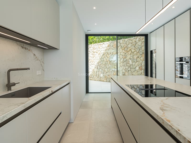 Cuisine moderne minimaliste avec armoires blanches, plans de travail en marbre et porte vitrée toute hauteur.