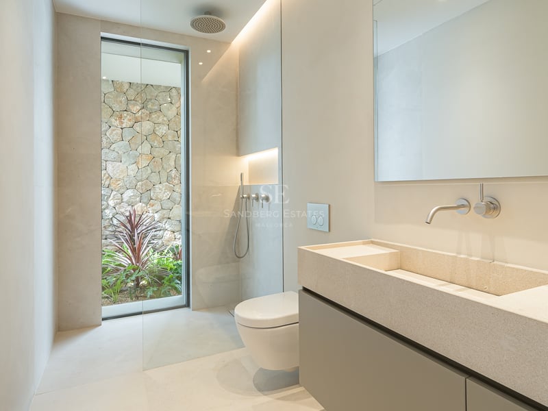 Salle de bain épurée avec double vasque en pierre, douche à l'italienne et fenêtre donnant sur un mur en pierre naturelle.