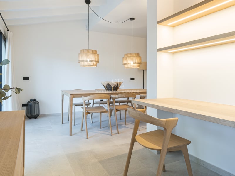 Salle à manger lumineuse avec table en chêne, bureau intégré avec étagères LED et sol en grès cérame.