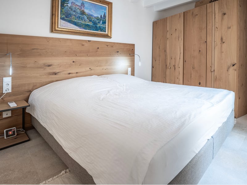 Chambre moderne avec grand lit, tête de lit et armoire en bois clair et un tableau classique.