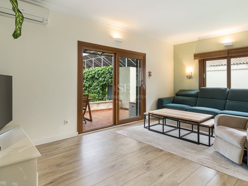 Salon lumineux avec canapé bleu canard, fauteuil, parquet et portes vitrées ouvrant sur une terrasse verdoyante.