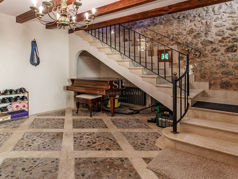 Hall d'entrée avec escalier en marbre, ferronnerie, mur en pierre apparente et piano à queue sous l'escalier.