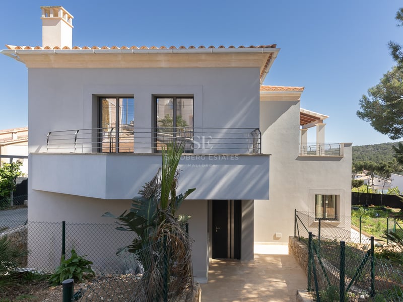 Villa moderne de deux étages avec façade blanche, tuiles en terre cuite et balcon sous un ciel bleu clair.