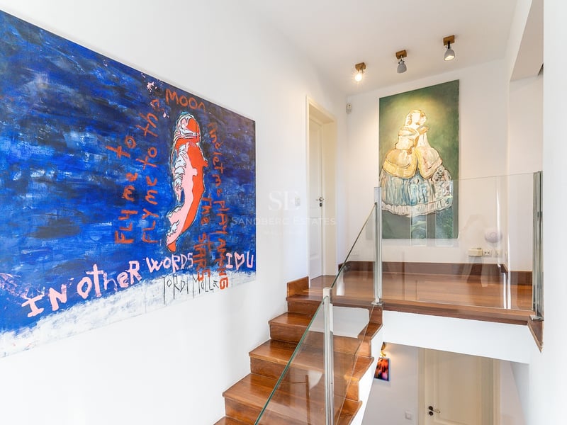 Escalier moderne en bois avec garde-corps en verre et grands tableaux abstraits sur murs blancs.