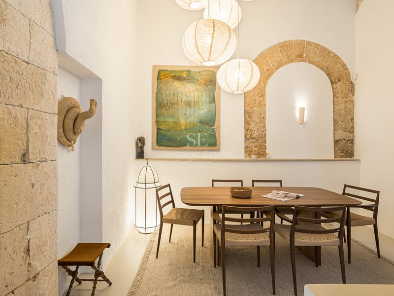 Table à manger moderne en bois et chaises sous des lanternes en papier dans une pièce avec une arche en pierre apparente.